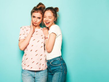İki güzel sarışın, gülümseyen yenilikçi kız, son moda hippi kot pantolon giyiyorlar. Mavi duvarın yanında poz veren kaygısız seksi kadınlar. Moda ve pozitif modeller eğleniyor.