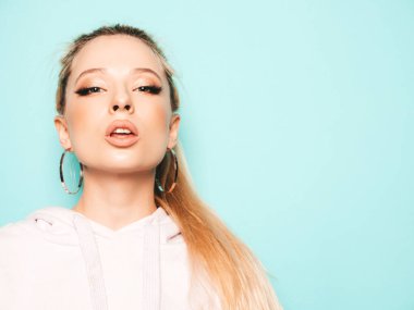 Yeni moda kot şort ve kapüşonlu kıyafetler giyen güzel, gülümseyen hippi kız portresi. Stüdyoda mavi duvarın yanında poz veren kaygısız seksi kadın. Pozitif model eğleniyor. 