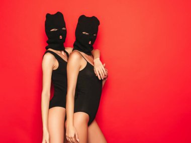 Siyah mayo giymiş iki güzel seksi kadın. Haydut maskesi takan mankenler. Stüdyoda kırmızı duvarın yanında poz veren seksi kızlar. Güzel iç çamaşırlı baştan çıkarıcı bir kadın.