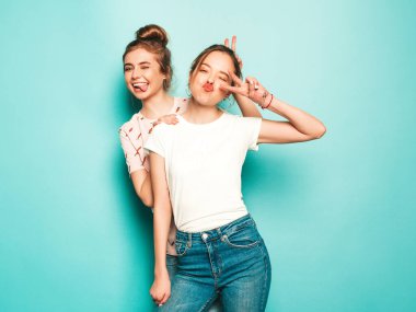 İki güzel sarışın, gülümseyen yenilikçi kız, son moda hippi kot pantolon giyiyorlar. Mavi duvarın yanında poz veren kaygısız seksi kadınlar. Moda ve pozitif modeller eğleniyor. Barış işareti gösteriyorlar.