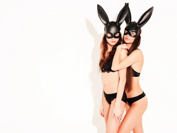 二つのセクシーな美しい女性はイースターバニーウサギのカーニバル黒マスクを身に着けています スタジオで白い壁の近くにポーズ熱いブルネットの女の子 素敵なランジェリーで誘惑モデル — ストック写真
