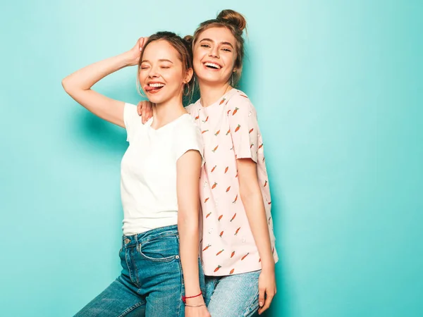 流行の夏のヒップスタージーンズの服で2人の若い美しいブロンドの笑顔ヒップスター女の子 青い壁の近くにポーズをとるセクシーな屈託のない女性 トレンディでポジティブなモデルが楽しい — ストック写真