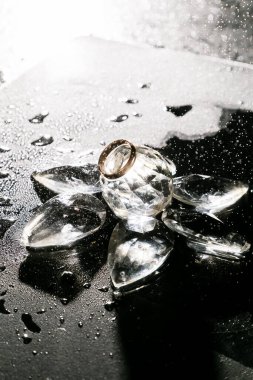 Buz küplerindeki altın alyans ışıldar ve yansıtır. Işığın yansımalarıyla su damlar. Odaklanma. Mücevher reklamı. Kavramsal moda mücevheri