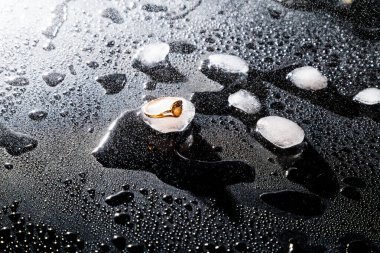 Su damlaları ve buz parçalarıyla siyah zemin üzerinde altın bir halka.