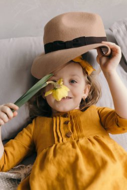 Sarı elbiseli küçük kız gülümsüyor ve narsist çiçekleri kokluyor.