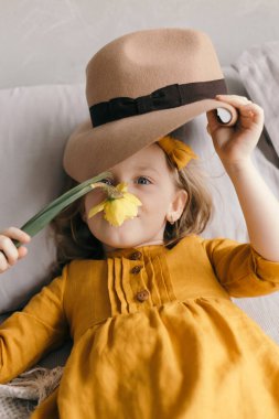 Sarı elbiseli küçük kız narsisli çiçeklerin tadını çıkarıyor.