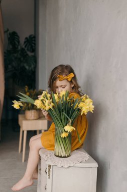 Sarı elbiseli küçük bir kız ve güzel bir buket narsist çiçek.
