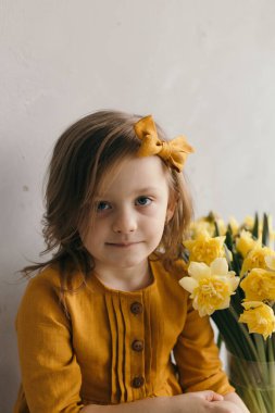 Sarı elbiseli küçük bir kız ve güzel bir buket narsist çiçek.