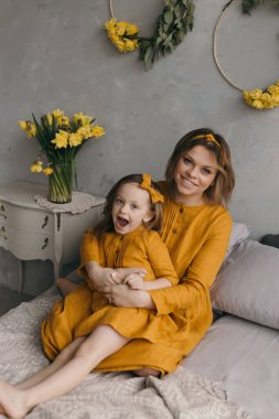 Anne kızının yatağında sarılıyor sarı güzel elbiseler içinde nergis çiçekli buketlerin yanında