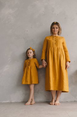 Sarı elbiseli anne ve kız duvarın yanında durmuş sarılıyorlar, eğleniyorlar.