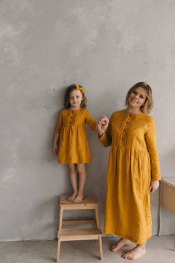 Sarı elbiseli anne ve kız duvarın yanında durmuş sarılıyorlar, eğleniyorlar.