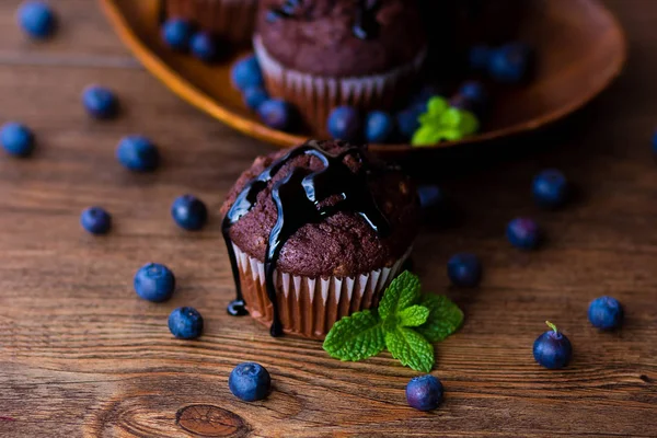 Schokoladenmuffins mit Schokoladensirup, Blaubeeren und Minze im Holzhintergrund — Stockfoto