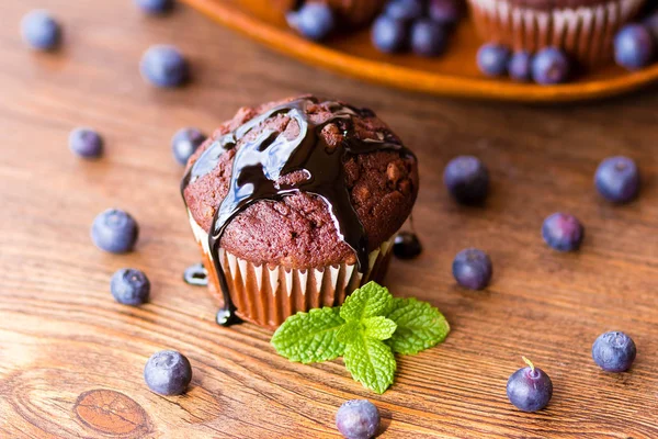 Schokoladenmuffins mit Schokoladensirup, Blaubeeren und Minze im Holzhintergrund — Stockfoto