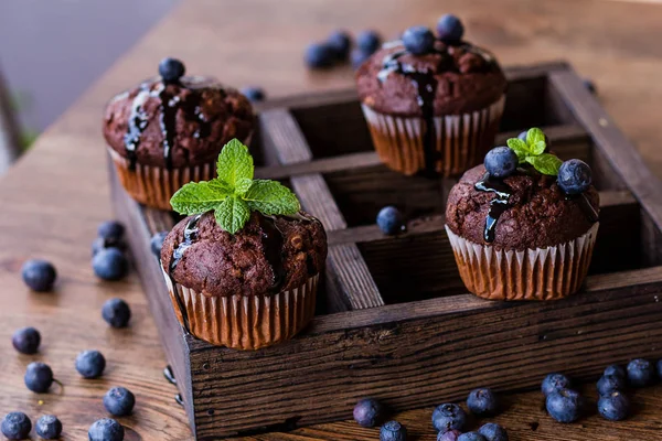 Magdalenas de chocolate con jarabe de chocolate, arándanos y menta en un fondo de madera —  Fotos de Stock