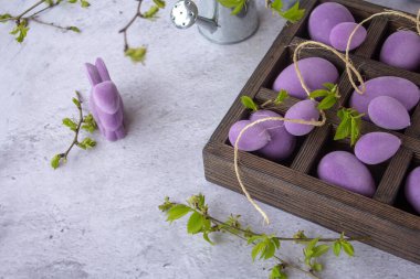 Ahşap bir kutuda mermer Paskalya yumurtaları, samandan bir yatakta, mor yapraklı erik ağacının çiçekli dalları.