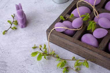 Ahşap bir kutuda mermer Paskalya yumurtaları, samandan bir yatakta, mor yapraklı erik ağacının çiçekli dalları.