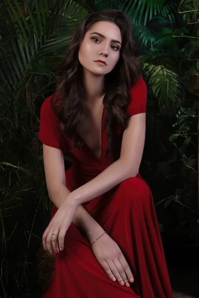 Дівчина в червоній сукні сидить у джунглях серед листя — стокове фото