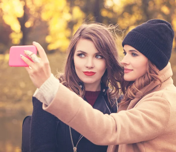 Chicas sonrientes felices con teléfono celular tomando selfie en Autumn Park — Foto de Stock