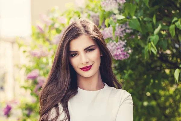 Hälsosamt leende kvinna med långt hår och smink på lila blommor — Stockfoto