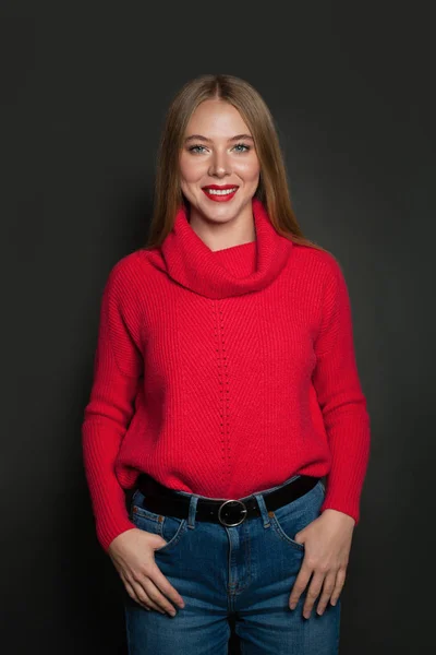 Mujer sonriente vistiendo suéter rojo sobre fondo gris. Emoción positiva —  Fotos de Stock