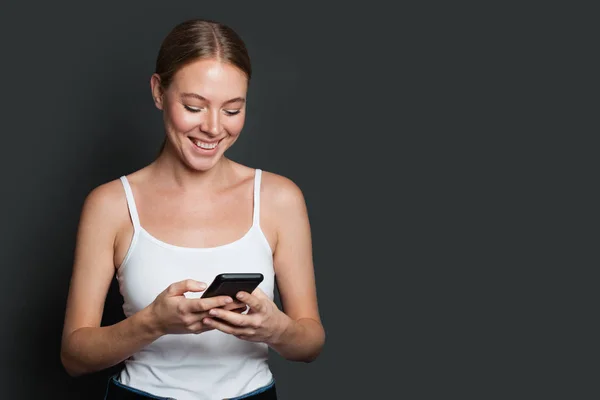 Joven mujer feliz usando el teléfono. Sonriente chica mensajes de texto en gris espalda — Foto de Stock