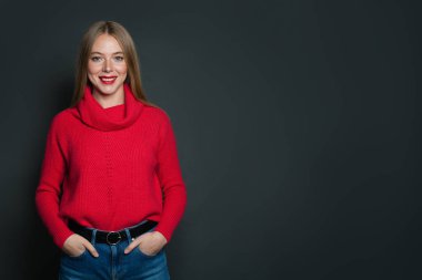 Kırmızı kazaklı mutlu kadın gri arka planda duruyor.