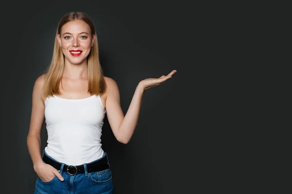 Felice giovane donna in piedi con la mano vuota aperta su sfondo grigio — Foto Stock