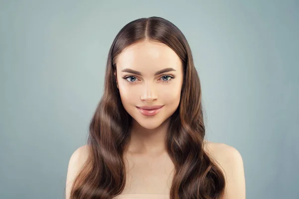 Hermosa mujer sana con cabello castaño largo sonriendo sobre fondo azul. Tratamiento facial, hidratante y cuidado de la piel —  Fotos de Stock