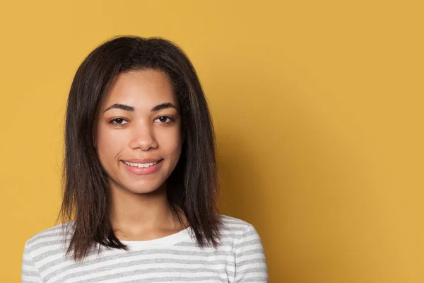 Smiling mixed race young woman in striped shirt on yellow studio — 스톡 사진