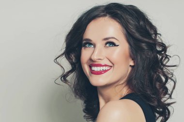 Cheerful brunette woman with curly hairstyle smiling on white 