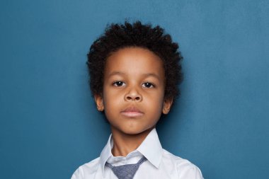 Portrait of curious smart black child boy student on blue background. African American kid pupil 6 years old