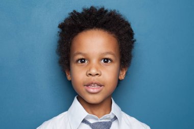 Little black kid boy student on blue background close up portrait