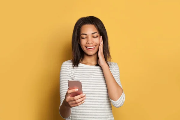 Niedliche schwarze Frau mit Handy und Spaß auf gelb — Stockfoto