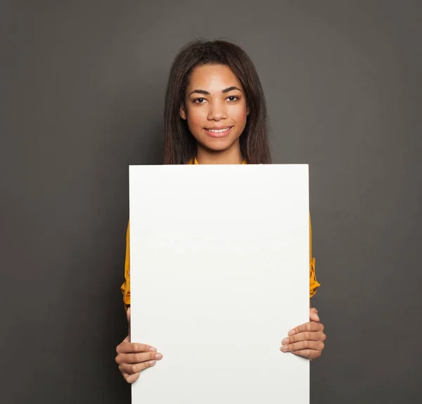 Щаслива чорна жінка тримає білу порожню вивіску на сірому фоні — стокове фото