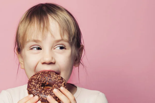 Enfant fille mordant beignet et regardant de côté sur fond rose — Photo