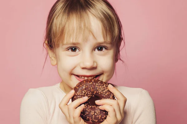 Bonne petite fille tenant beignet au chocolat sur fond rose — Photo