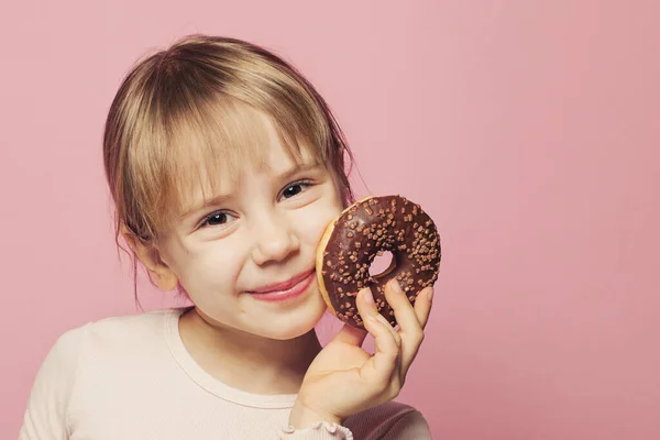 Adorable petite fille tenant beignet au chocolat sur rose — Photo