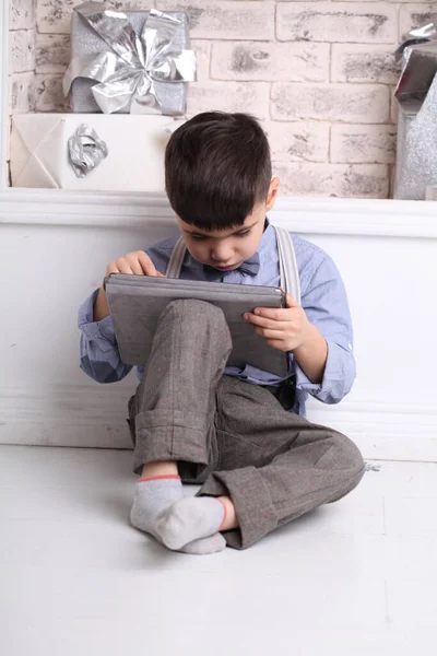 Gelukkige jonge jongen zit op de vloer met behulp van een tablet. — Stockfoto
