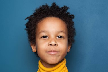 Afro-Amerikalı çocuk mavi arka planda yakın plan çekimleri yapıyor.