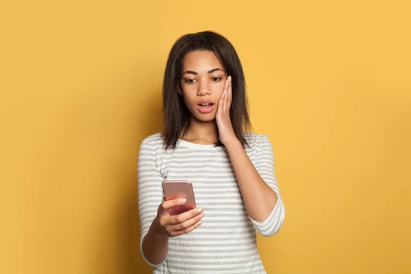 Schockierte Schwarze Frau Blickt Auf Handy Auf Gelbem Hintergrund — Stockfoto