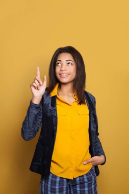 Siyahi bir kız öğrenci, parlak sarı arka planda işaret ediyor.