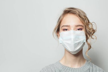 Gri arka planda yüz maskesi takan genç bir kadın. Grip salgını ve virüs koruma kavramı