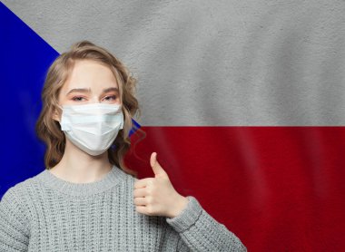 Yüz maskeli mutlu kadın, Çek Cumhuriyeti bayrağının arka planında başparmak kaldırıyor. Grip salgını ve virüs koruma kavramı