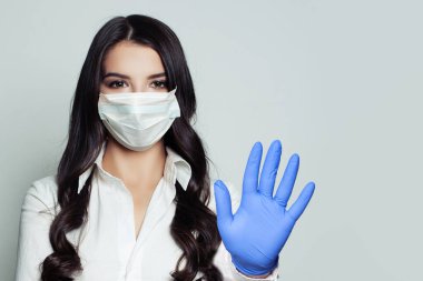 Tıbbi maske takan genç bir kadın pandemik jesti durdurduğunu gösteriyor. Güvenlik maskeli ve tıbbi eldivenli bir kadın. Grip salgını ve virüs covid-19 koruma kavramı