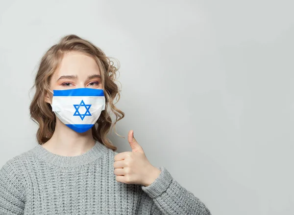 戴面具的快乐女人举着大拇指 有以色列国旗的背景 流感流行与病毒防护概念 — 图库照片