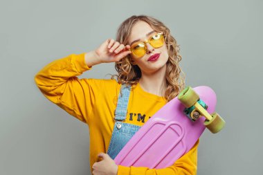 Güneş gözlüklü mutlu kadın beyaz arka planda pembe kaykay tutuyor.