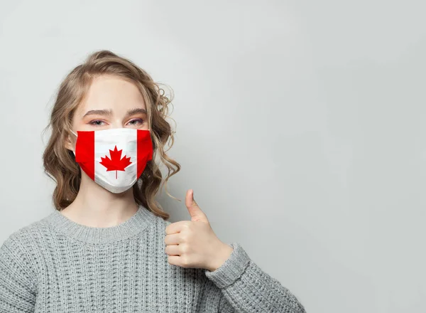 戴面具的快乐女人举着大拇指 有加拿大国旗的背景 流感流行与病毒防护概念 — 图库照片