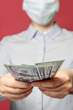 Tıbbi maskeli kız elinde para tutuyor. Mavi arka planda bize dolar veriyor.