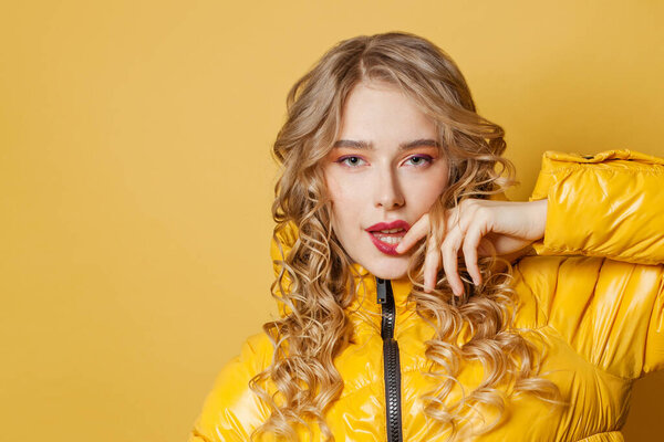 Портрет красивой молодой женщины в желтой зимней куртке на ярко-желтом фоне
