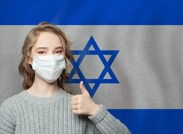 戴面具的快乐女人拿着大拇指站在以色列国旗的背景上 流感流行与病毒防护概念 — 图库照片